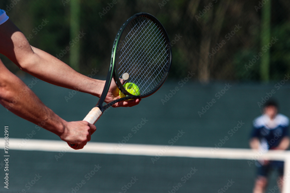 Detail of young boy with racket playing tennis on a clay court during a university tournament. the athlete is wearing a blue sports t-shirt and is preparing to serve for set point