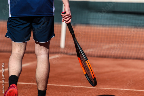 A young boy with racket playing tennis on a clay court during a university tournament. the athlete is wearing a blue sports shirt.