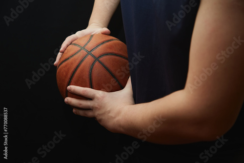 The hands of a basketball player hold the ball to the side, shielding the ball in basketball