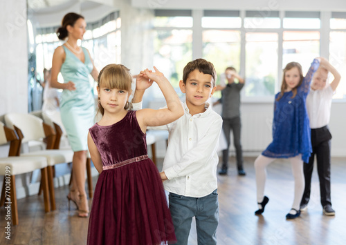 Joyful schoolboys and schoolgirls of primary classes training valse dance in events salon