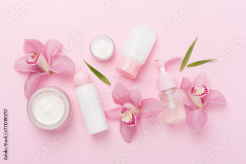 Bottles and jars with cream and orchids on color background, top view