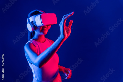 Smart female standing with surrounded by cyberpunk neon light wear VR headset connecting metaverse, futuristic cyberspace community technology. Woman using hand touching virtual object. Hallucination. © Summit Art Creations