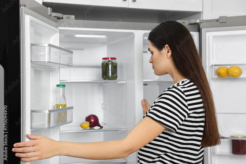 Upset woman near empty refrigerator in kitchen Upset woman near empty refrigerator in kitchen