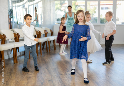 Happy little children in elegant dresses practicing twist dance with teacher in school hall