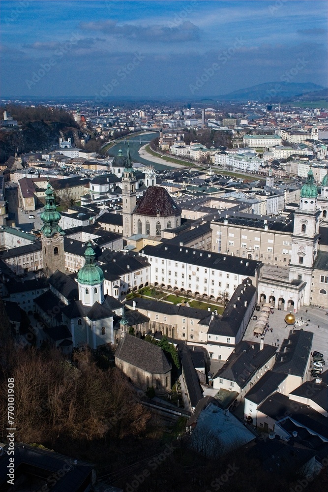 Aerial view of a historic European city with prominent cathedrals and buildings, under a clear sky.