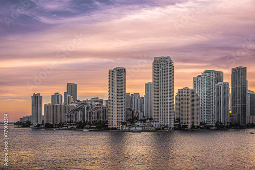 Miami  Florida  USA - July 29  2023  Warm colored sky over buildings on Brickell Key island at evening 19 43. The Centinel statue between Tequesta points on the shoreline. Green foliage