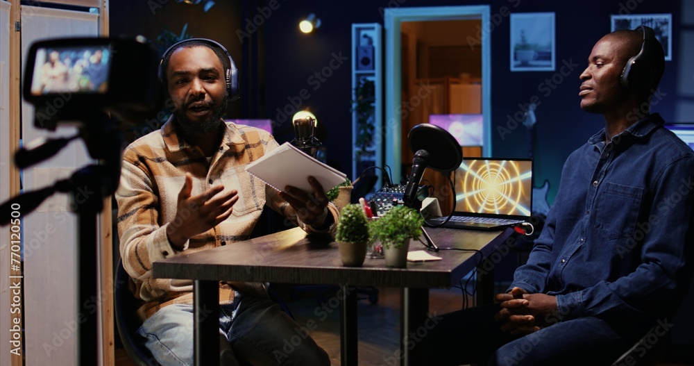 Cohosts streaming podcast using professional vlogging gadgets to live broadcast debate on politics vlog channel. Men meeting in neon lights decorated living room studio to film show