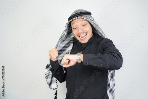 Asian Muslim man wearing Arab turban sorban excited face expression looking at watch in copy space photo