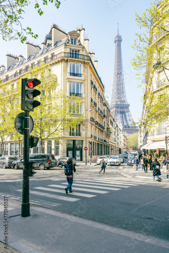 Fototapeta Naklejka Na Ścianę i Meble -  Pedestrians walk near a street corner with the Eiffel Tower in the background on a clear day. Paris, France