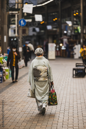 An elderly woman wearing a kimono walks down the center of a shopping street in Kobe, Japan