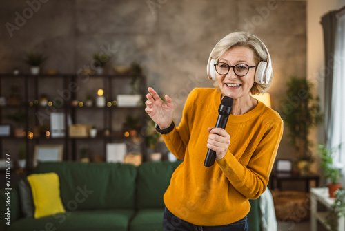 Fotografie One woman mature blonde hold microphone at home happy smile sing dance