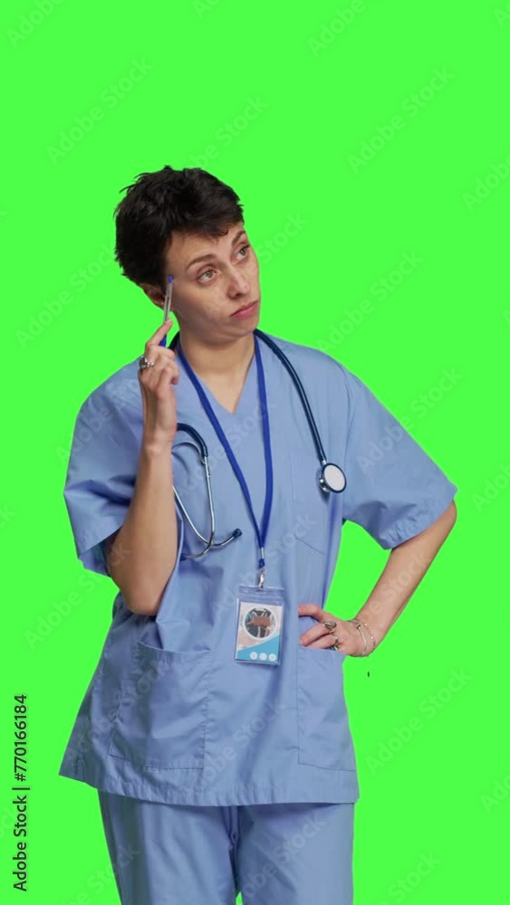 Front view Medical assistant thinking about new treatment ideas in studio, acting thoughtful while she stands against greenscreen backdrop. Pensive young nurse contemplating about healthcare ideas Front view Medical assistant thinking about new treatment ideas in studio, acting thoughtful while she stands against greenscreen backdrop. Pensive young nurse contemplating about healthcare ideas