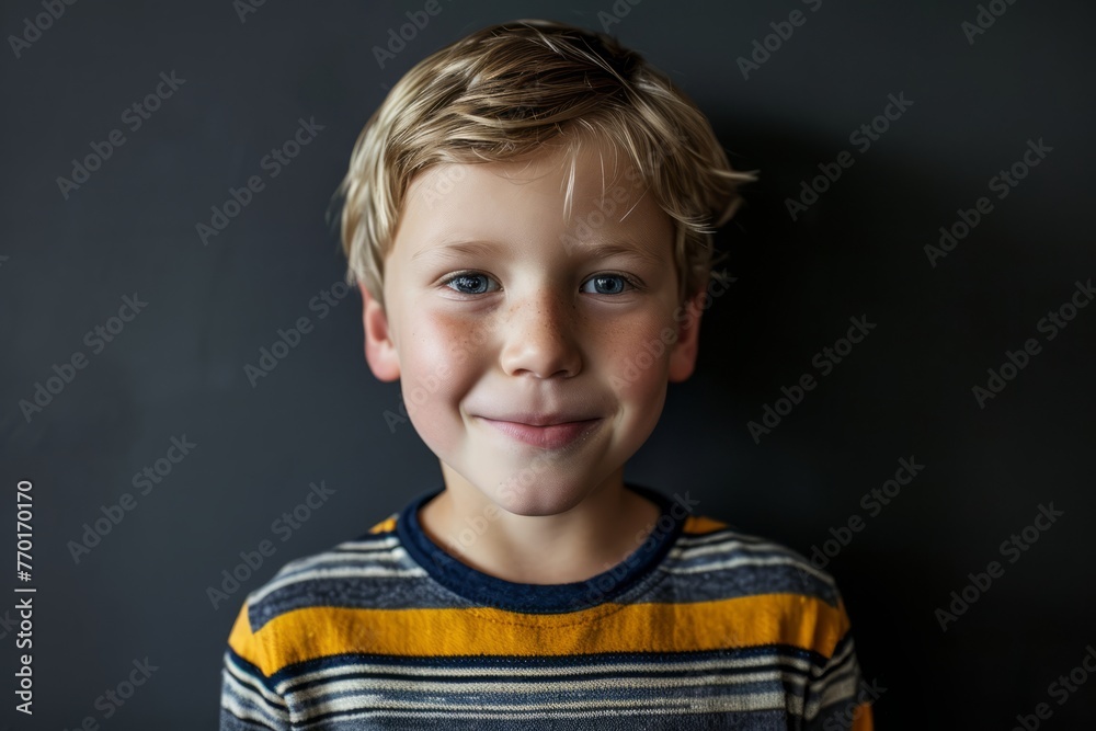 Cute little boy with blond hair and blue eyes, looking at camera and smiling, against grey background Cute little boy with blond hair and blue eyes, looking at camera and smiling, against grey background