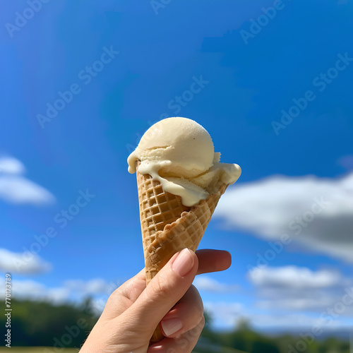 hand holding waffle cone with scope of vanilla ice cream against blue sky