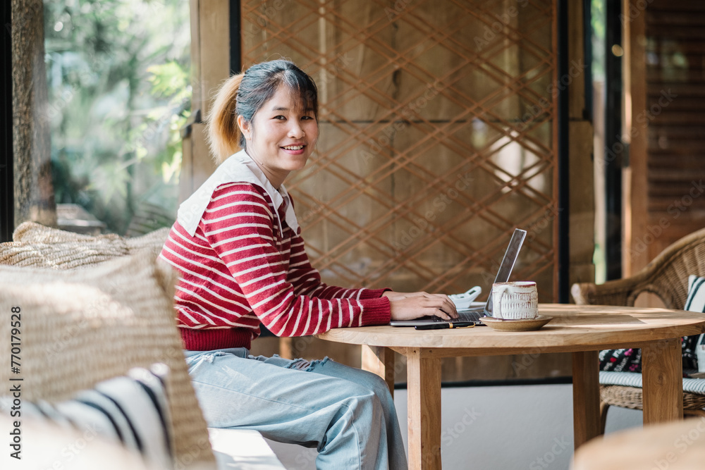 Freelancer smiles while working on her laptop at a rustic wooden table, with a cozy atmosphere and natural backdrop. Freelancer smiles while working on her laptop at a rustic wooden table, with a cozy atmosphere and natural backdrop.