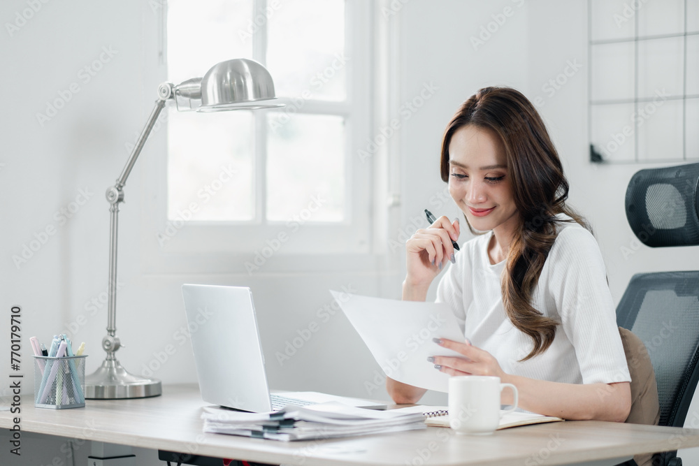 Smiling businesswoman in a bright office reviewing documents with a pen in hand, showing efficiency and focus in her professional routine. Smiling businesswoman in a bright office reviewing documents with a pen in hand, showing efficiency and focus in her professional routine.