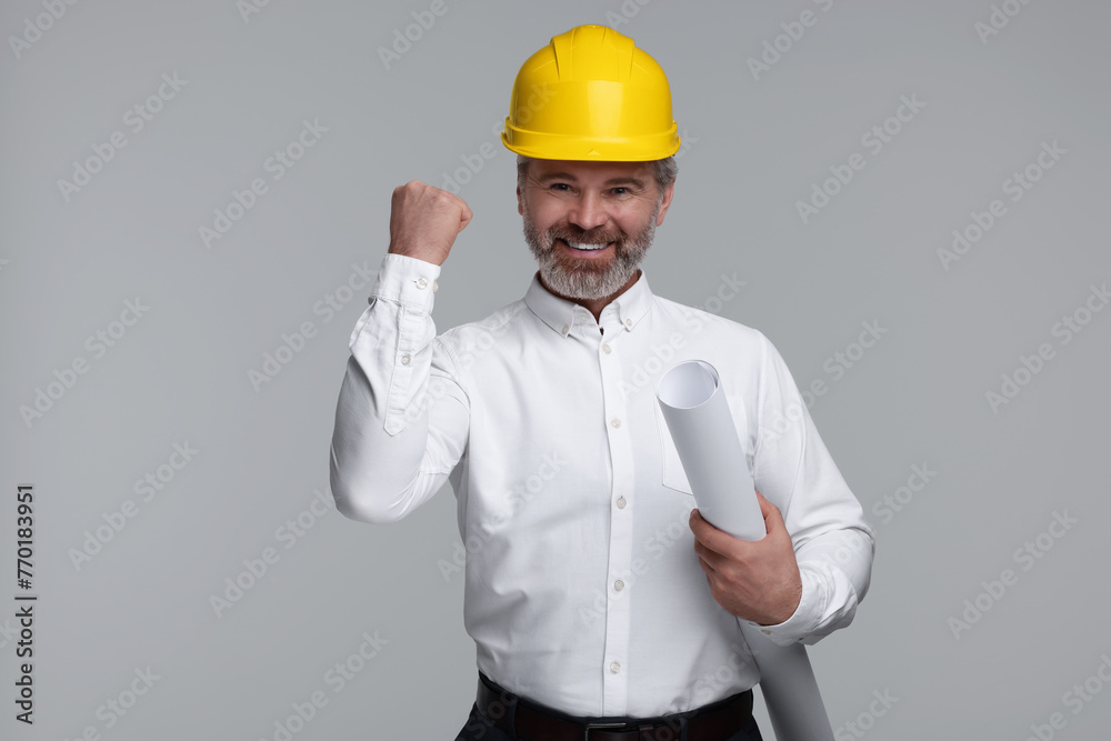 Architect in hard hat holding draft on grey background Architect in hard hat holding draft on grey background