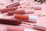 Different lip glosses, applicators and flowers on pink background, closeup