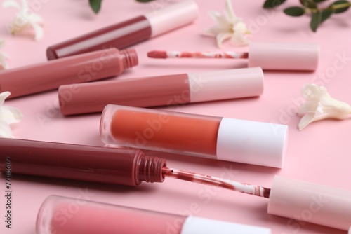 Different lip glosses, applicators and flowers on pink background, closeup
