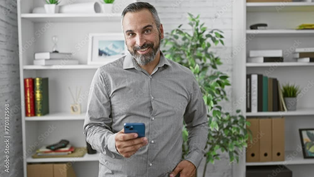Confident senior hispanic man with beard and grey hair giving a thumbs up in a modern office setting.