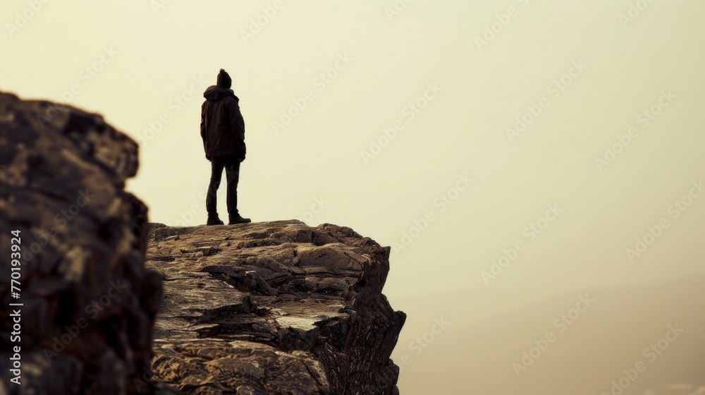 A solitary figure stands on a rocky ledge back to the viewer gazing out towards the horizon. The rugged terrain and the figures . .