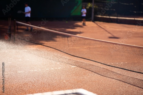 friends playing tennis on a clay court, watering and bagging a clay court. doing tennis court maintence photo