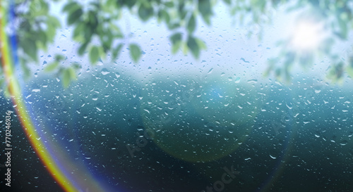 梅雨 雨の滴のついた窓ガラスと前面の木の葉とレンズフレア太陽の日差しの背景 ガラス越し奥の山林・森林の風景 6月・梅雨明け・水滴・日本・季節