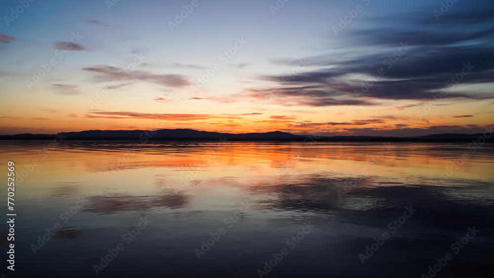 Beautiful sunset overlooking a quiet lake and mountains. The golden hour, a mirror image on the water. Beauty is in nature.