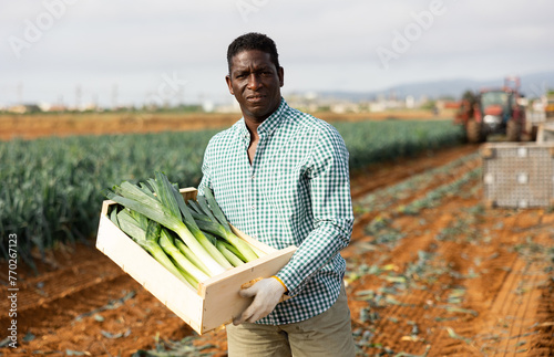Male seasonal worker posing with freshly picked leek on vegetables farm land