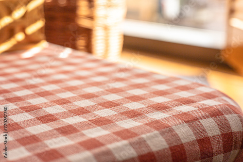 Close up of red and white checkered tablecloth on the table near the window, selective focus. Copy space to display visual content,