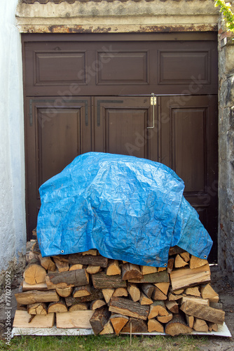 Covered firewood in a pile in front of a gate in the yard.