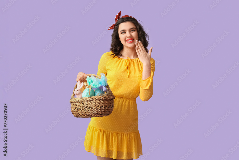 Beautiful pin-up woman holding Easter basket on lilac background