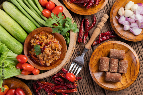 Sweet pork in a wooden bowl with cucumber, long beans, tomatoes, and side dishes.