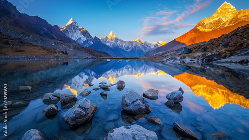 Beautiful landscape with high mountains with illuminated peaks, stones in mountain lake, reflection, blue sky and yellow sunlight in sunrise. Nepal. Amazing scene with Himalayan mountains.