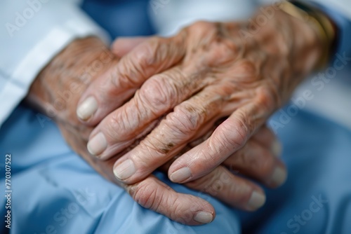 Close-up of an elderly person's hands clasped by a person in a blue medical uniform.