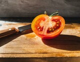 A vibrant, ripe tomato freshly sliced, its juicy interior glistening on a rustic wooden cutting board, with a gleaming knife beside it