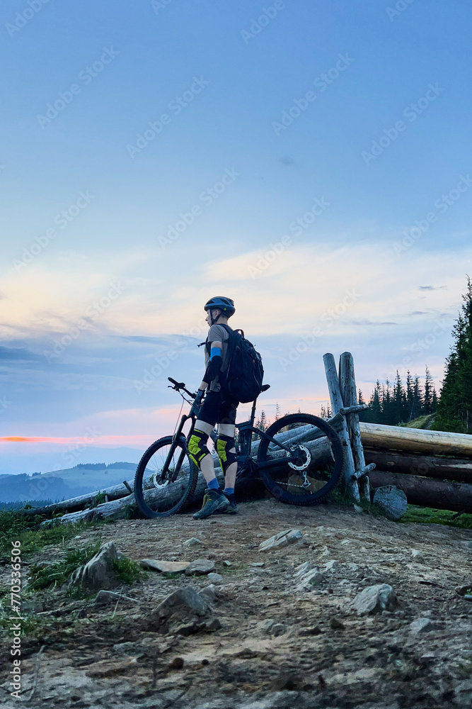 Cyclist man riding electric bike outdoors in the evening. Male tourist resting on hill, enjoying beautiful mountain landscape, wearing helmet and backpack. Concept of active leisure.