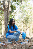 A cute young woman holds a garbage bag and a group of Asian volunteers collect garbage in plastic bags and clean up the area in the forest to preserve the natural ecosystem.