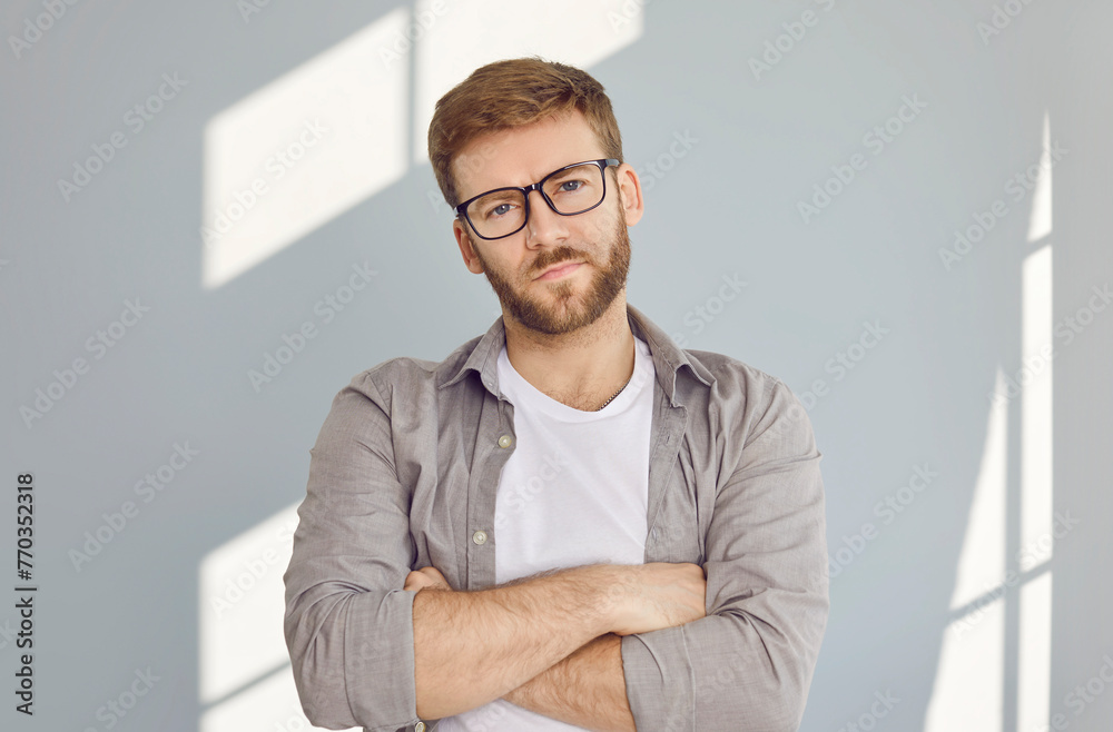 Portrait of confident serious bearded handsome man in glasses standing with crossed arms wearing white t-shirt and beige shirt isolated on grey wall background. Smart guy looking at the camera. Portrait of confident serious bearded handsome man in glasses standing with crossed arms wearing white t-shirt and beige shirt isolated on grey wall background. Smart guy looking at the camera.
