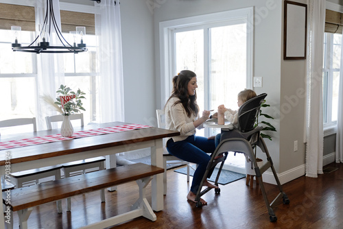 Woman feeding baby lunch while she sits in high chair photo