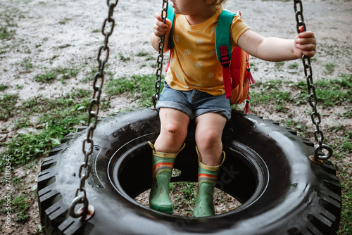 Colorfully dressed child sitting on tire swing on rainy day photo