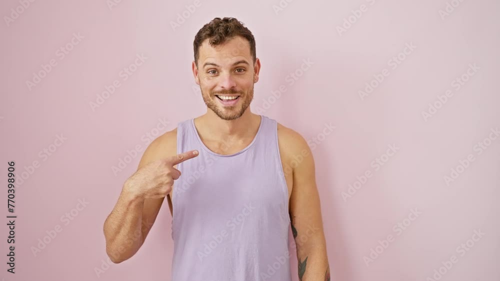Spirited young man in a sleeveless t-shirt beaming joyfully, confidently pointing with finger over isolated pink background Spirited young man in a sleeveless t-shirt beaming joyfully, confidently pointing with finger over isolated pink background