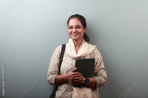 Woman of Indian ethnicity with a smiling face holding a tablet computer in hand