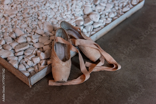Pair of used ballet slippers rests on pebble-covered surface, hinting at the rigorous practice behind a dancer's journey.