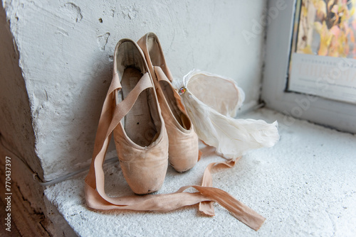 Well-used pointe shoes with ribbons, white feather tiara lie beside window, telling story of dedication and the graceful art of ballet.