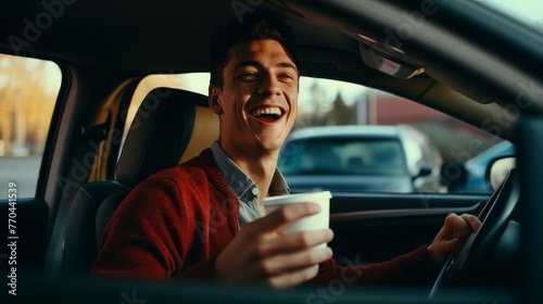 Portrait of a laughing man drinking coffee from a disposable cup while driving a car © Nadzeya
