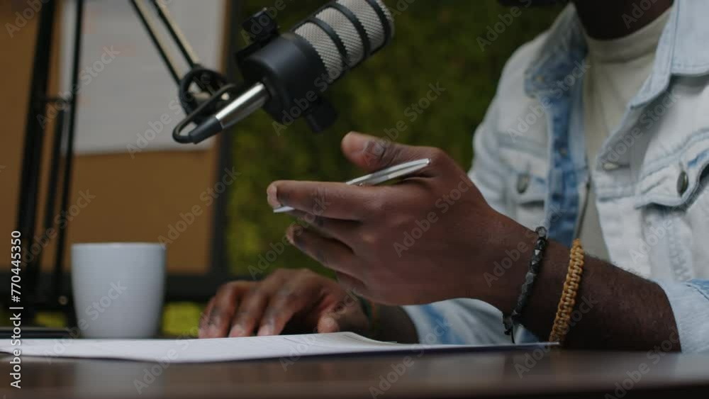 Close up view of African American podcast host holding pen and gesturing as talking in mic at desk in recording studioClose up view of African American podcast host holding pen and gesturing as talkin Close up view of African American podcast host holding pen and gesturing as talking in mic at desk in recording studioClose up view of African American podcast host holding pen and gesturing as talkin