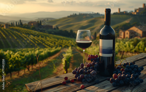 A bottle of red wine, blank label, with glass of red wine on a wooden table with bunches of grapes and on the background vineyards and hills. Natural soft and warm lighting