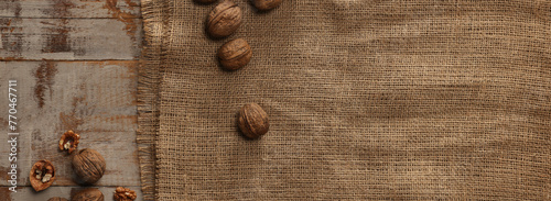 Burlap fabric and walnuts on wooden table, top view. Space for text