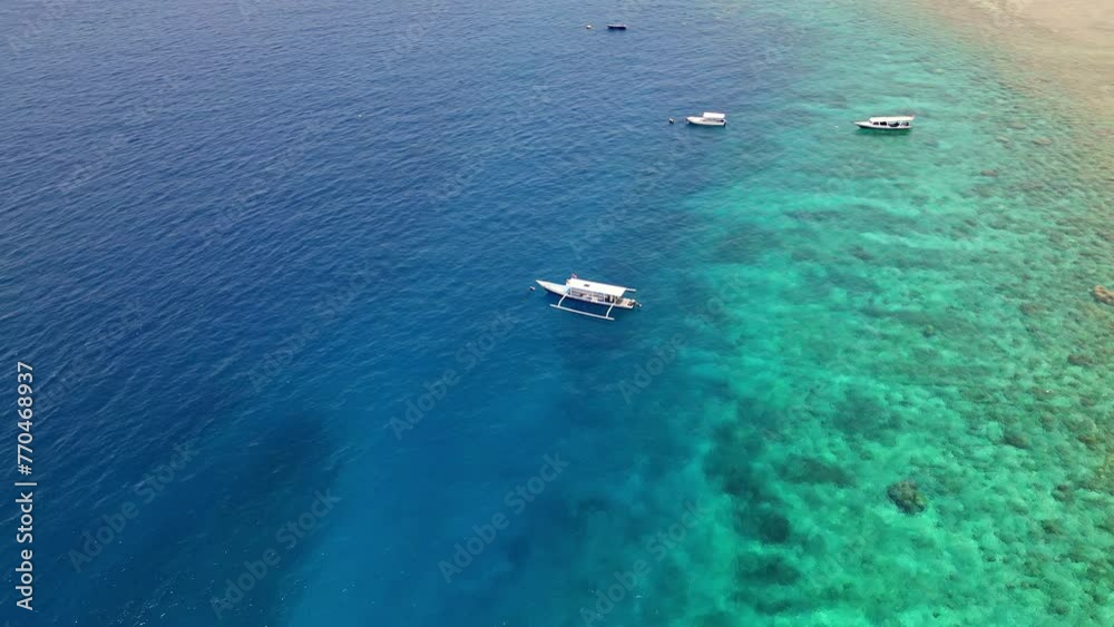 Aerial view orbiting tourist boats on the edge of a fringing coral reef and tropical island